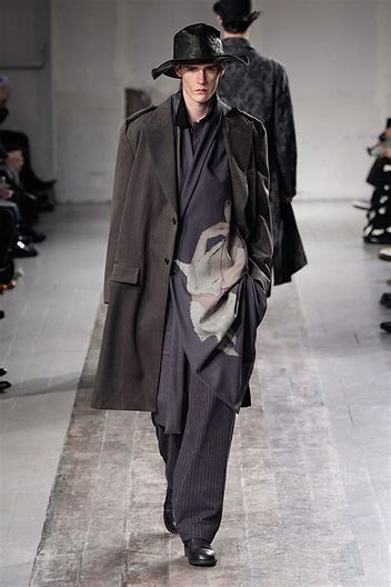 Model on the Yohji Yamamoto Fall/Winter 2024 runway wearing a draped black turtleneck and wide-leg charcoal trousers, highlighting the designer’s signature monochromatic palette and fluid, deconstructed silhouette.
