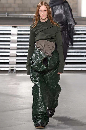 Model walking the Rick Owens Fall 2017 menswear runway in a layered, sculptural ensemble featuring exaggerated silhouettes and muted earth tones, embodying the designer’s dark, avant-garde aesthetic.