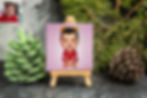 Cartoon portrait of a baby wearing a red outfit and bear ears, on a custom miniature easel