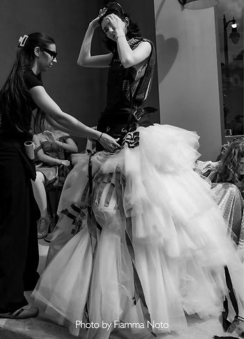 Black-and-white backstage photo of a SCAD student designer adjusting a model’s dramatic layered tulle gown moments before the runway presentation.