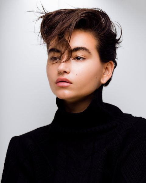 Model with short dark hair in black sweater, septum piercing.
