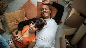 Smiling couple lying on the floor among moving boxes, holding hands.