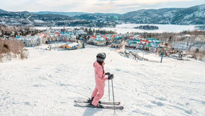 Person skiing down a snowy slope overlooking a colourful mountainside village and winter resort landscape.