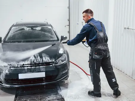 Male worker in uniform washing new modern car that covered with soap. Conception of service