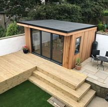 Contemporary cedar-clad garden room and landscaping project completed in Keighley, West Yorkshire, featuring natural timber decking, stepped seating, aluminium sliding doors and a paved patio area.