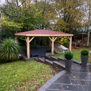 Wooden pyramid gazebo to provide shelter for the hot tub with red shingle roof in a garden