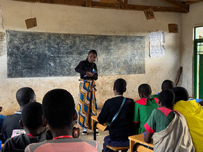 Malawian teacher standing in front of a blackboard, with several pupils at desks.