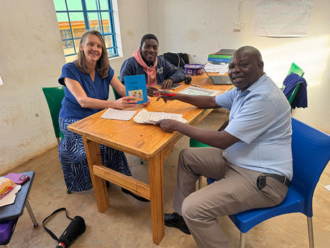 Three adults sitting at a desk with children's school books.