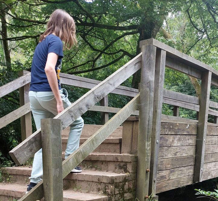 Mijn zoon loopt een bruggetje op. Je ziet van de achterzijde. Hij is een smalle jongen, draagt een lichte joggingbroek met een donker t-shirt.