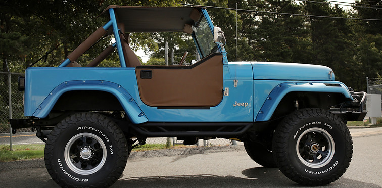 Blue Jeep CJ7 with brown soft top and doors on large off-road tires at Angels Touch Restoration.