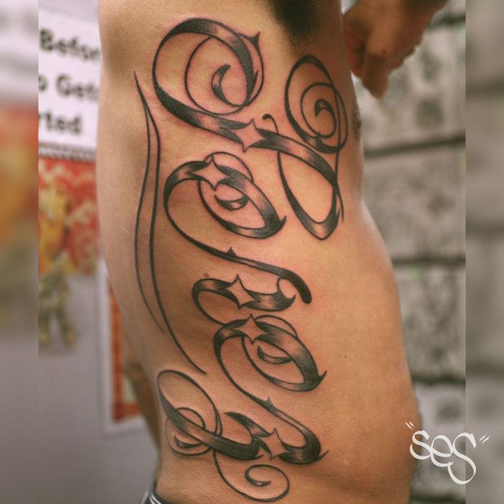 Custom Chicano style script lettering tattoo on rib cage by Ses at Blackwork Tattoo Studio in Little Falls, NJ
