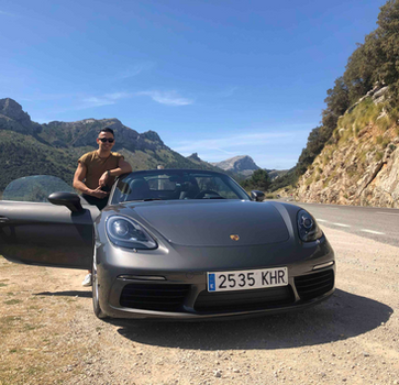 Dark silver Porsche 718 Boxster parked on a quiet Pyrenees mountain road with rugged peaks behind.