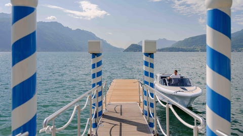 Motorboat approaching a wooden jetty with blue-and-white posts on Lake Como.
