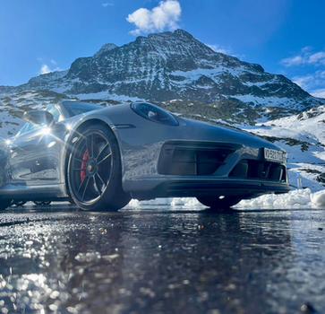 Silver Porsche 911 convertible parked on a snowy mountain pass, sparkling in the sun on a Swiss Alps luxury driving tour.