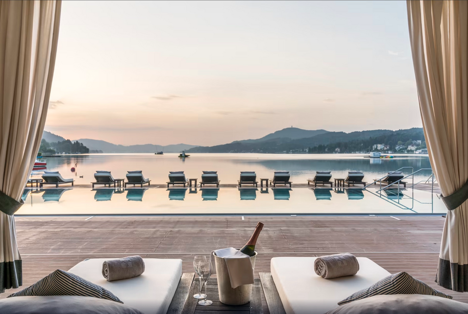 Infinity pool with loungers overlooking Lake Wörthersee at Falkensteiner Schlosshotel Velden, perfect sunset stop on the Alps-to-coast route.