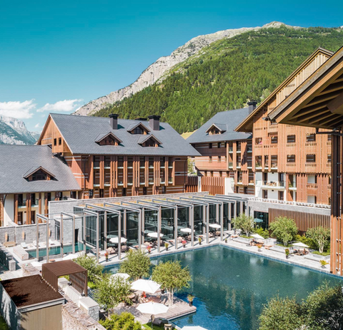 Exterior of The Chedi Andermatt luxury hotel with outdoor pools and terraces framed by Swiss Alpine mountains.