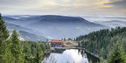 Lake Mummelsee in Germany’s Black Forest with a lakeside hotel surrounded by dense fir trees and misty hills.