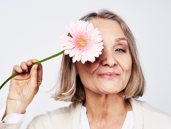 Cheerful elegant elderly woman holding a flower near the face on a gray background.jpg