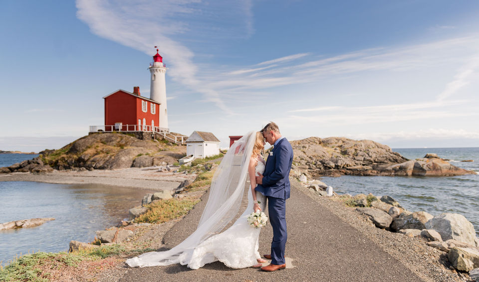 Bride & Groom stand foreheads together in front of Fisguard Lighthouse gleaming red against the blue sky