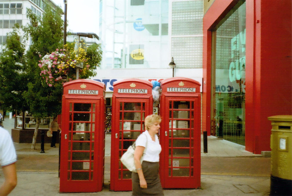 A woman walks past three classic red London telephone boxes on a busy street, captured in a candid disposable camera style.