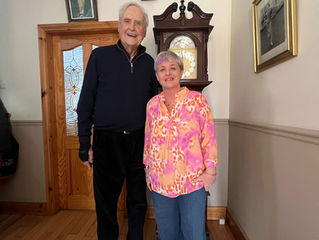 “91 year old homeowner Mick standing smiling beside his Home Share companion Brenda in his home in Ireland, showing companionship, support and independent living in later life.”