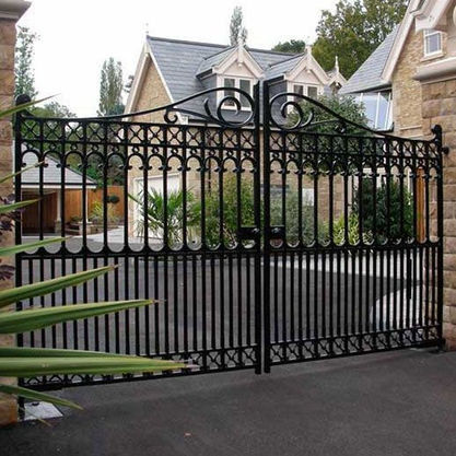 Ornate welded scrolls adorn a large driveway gate, which features double doors that are automatic, enhancing safety and ensuring privacy with a secure design. custom welded by welder in fabrication shop in Santa Barbara
