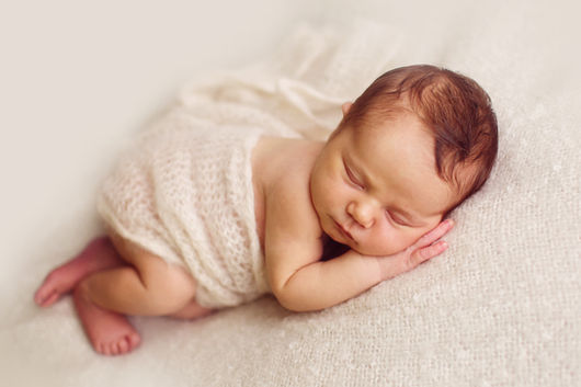 Pasgeboren baby slapend op een wit dekbed bij het raam