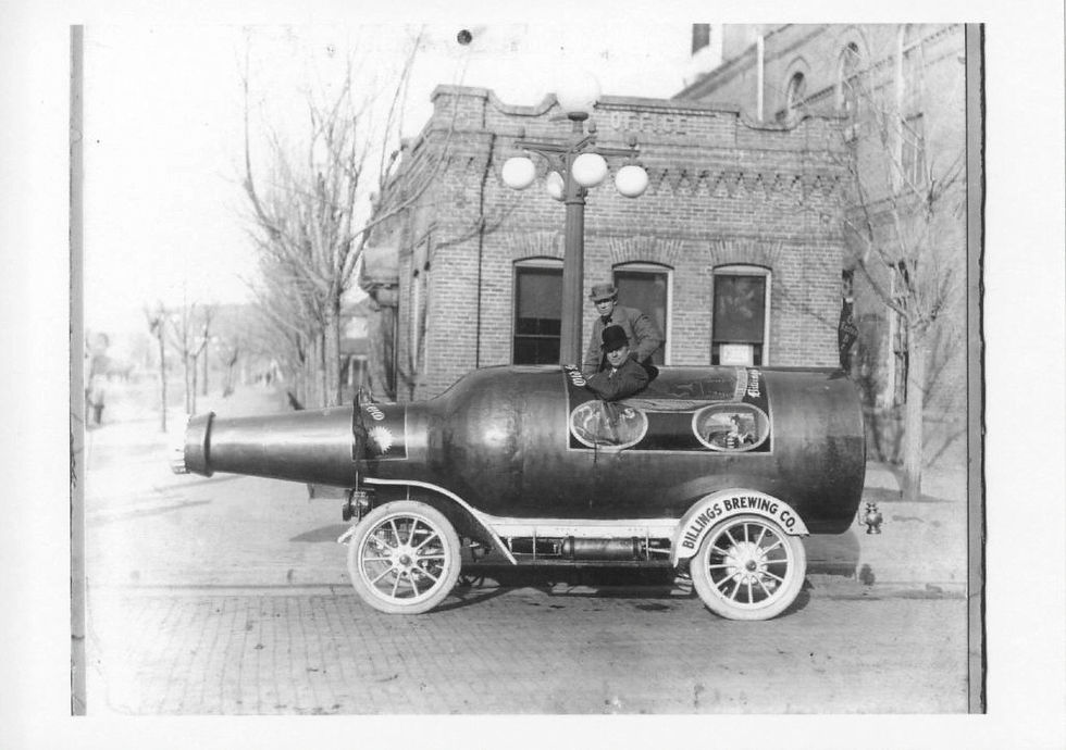 Vintage Billings Brewing Company photo shows two workers in a beer-bottle-shaped car with two men, parked on a street before a vintage Billings building