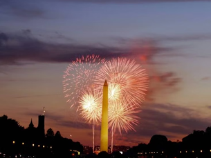 Fireworks burst behind the Washington Monument at dusk, with a glowing sunset sky. This year's fireworks display is the largest in history.
