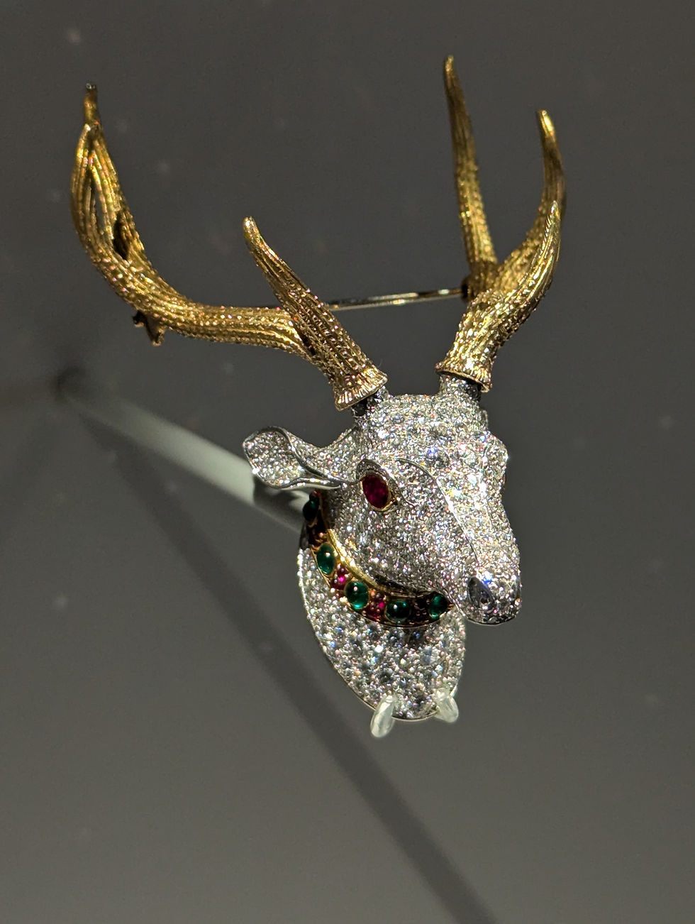 Sparkling jeweled deer head brooch by Cartier, with exquisite gold antlers and red-and-green gems on a dark display background.