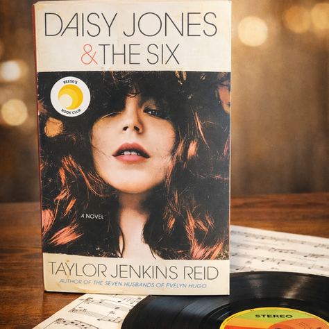 Book cover of Daisy Jones & The Six by Taylor Jenkins Reid, featuring a woman's face. A vinyl record and sheet music in the background.