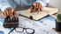 A financial professional uses various tools and spreadsheets at their desk.