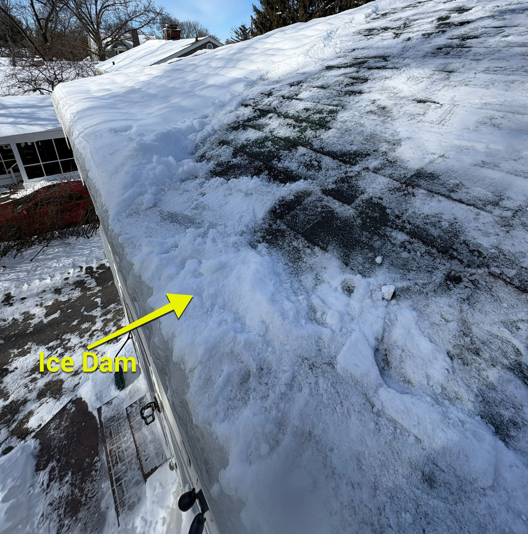 Thick snow and ice buildup forming an ice dam along the eaves of a residential roof during a winter freeze.