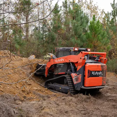Track loader clearing brush and soil near trees on private property in Georgia.