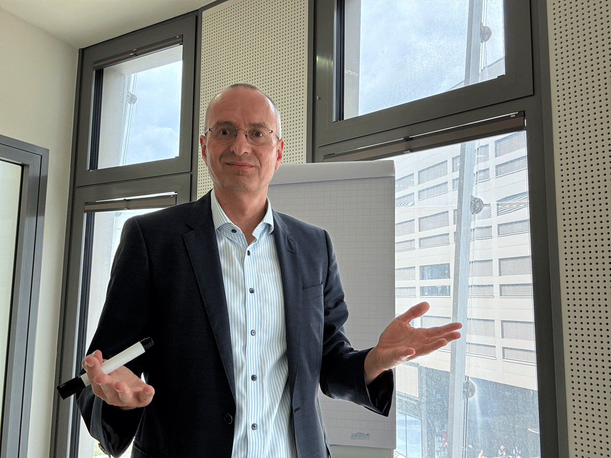 Coaching-Szene mit Oliver Wunsch im Büro – in Interaktion vor dem Flipchart, offener Gestus und positiver Ausdruck. Steht für Klarheit, Transformation und lösungsorientierte Arbeit.