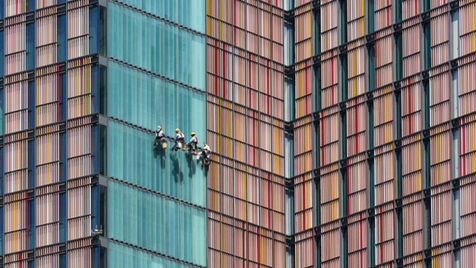 Workers cleaning a tall building with a vibrant glass exterior