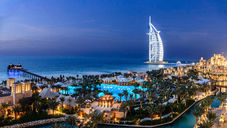 Burj Al Arab hotel and Madinat Jumeirah resort in Dubai at night, with the sail-shaped hotel illuminated against the dark sky, surrounded by pools, canals, and palm trees