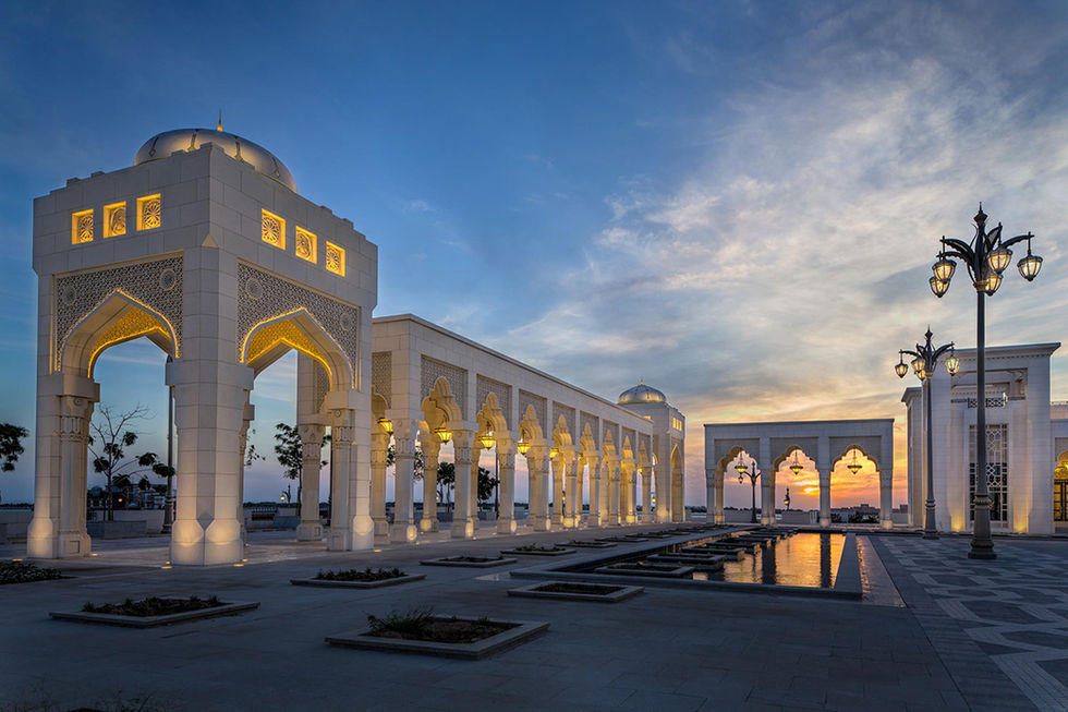 Qasr Al Watan palace arches illuminated at dusk with reflection.