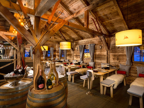 Rustic wooden Alpine chalet with a dark grey roof, designed for a cozy winter dining experience in a charming mountain setting.