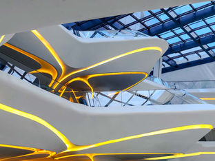 Interior of the lobby at ME Dubai in The Opus, showcasing sculptural white curved balconies, glowing yellow integrated lighting, and a glass atrium roof.