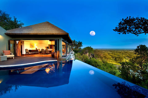 Luxurious villa at Bilila Lodge in the Serengeti, Tanzania featuring an infinity pool overlooking the savanna, with a view of the moonlit sky and the lodge’s elegant interior.