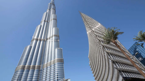 Low-angle view of the Burj Khalifa and a curved modern skyscraper against a clear blue sky in Dubai