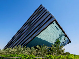 Modern glass building against a clear blue sky with nearby palm trees