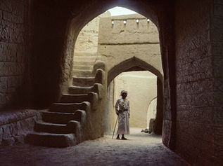 Man in traditional dress standing in an ancient archway with stone steps.