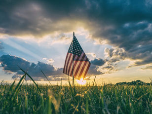 An American flag in a field while the sun set behind it.