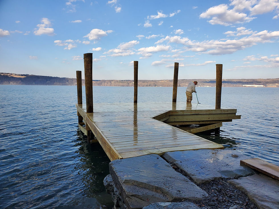 Man working on new wooden dock extending into blue lake water.