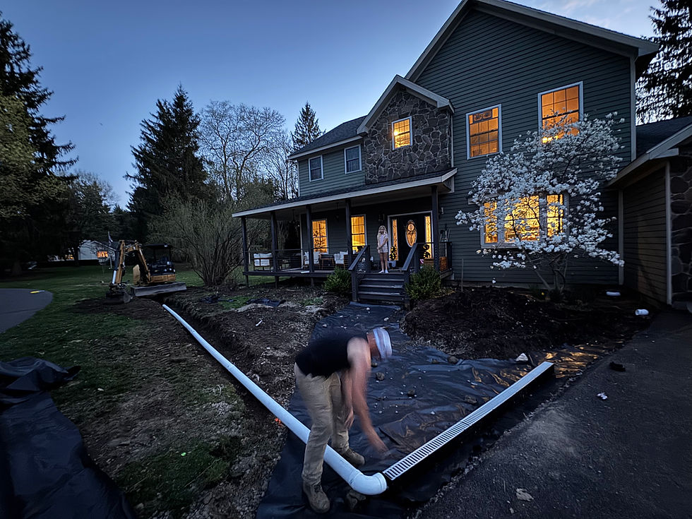 Man installing drainage pipes around house with landscape fabric at dusk.