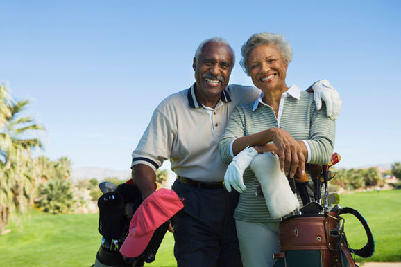 Smiling couple on golf course with golf bags beside them enjoying a sunny day.