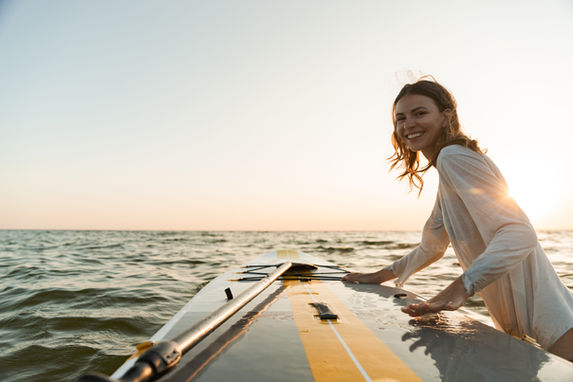 Smiling woman on a paddleboard on the ocean during a beautiful sunset.