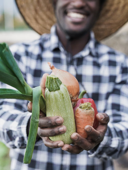 Smiling man holding fresh vegetables in hand, field background, farm produce